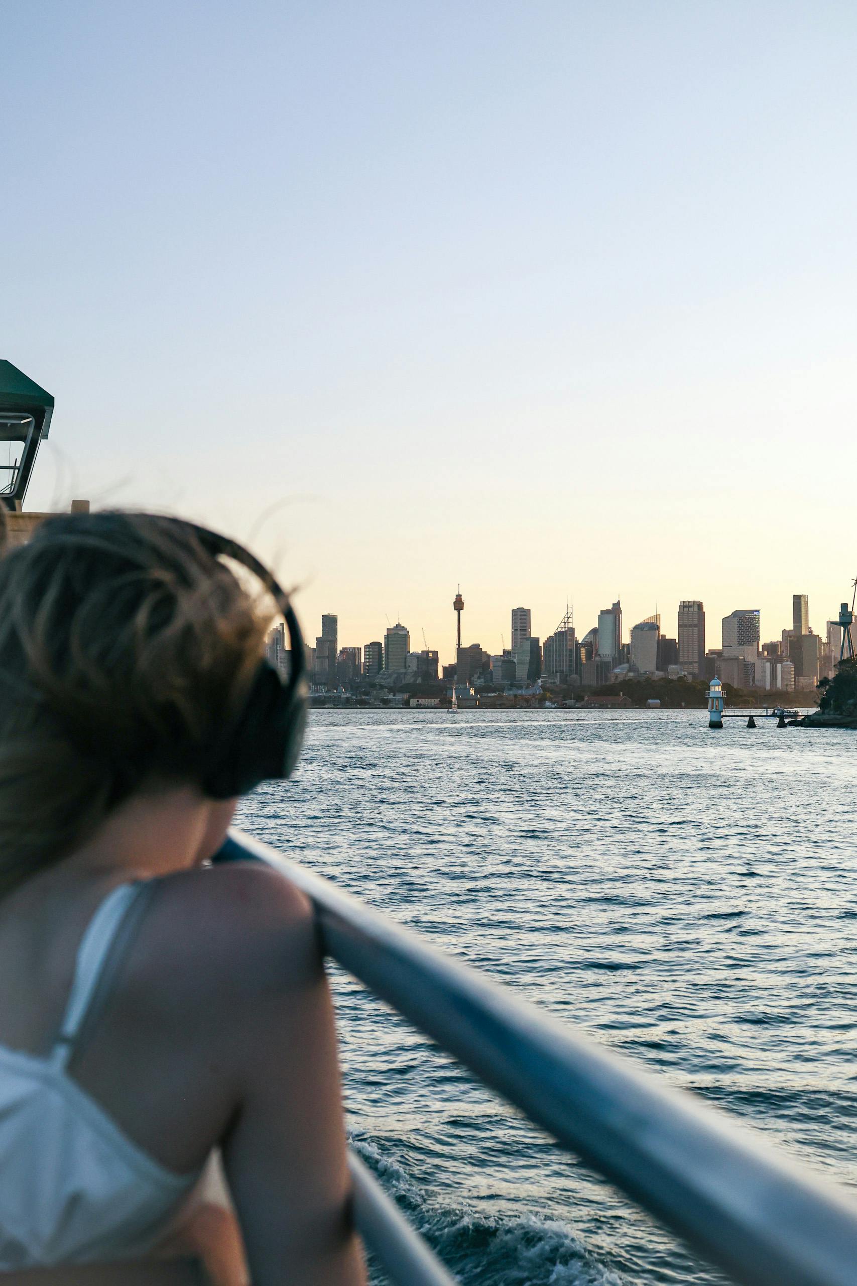 A woman listens to music while viewing Sydney Harbour and skyline at sunset.