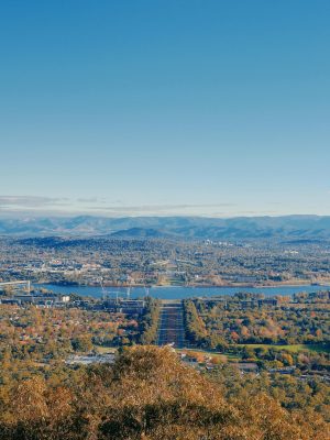 A breathtaking aerial view of Canberra city with mountains and vibrant autumn foliage under a clear blue sky.