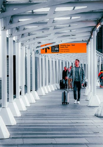 Travelers walking through a modern airport walkway with luggage, heading towards a taxi pickup point.