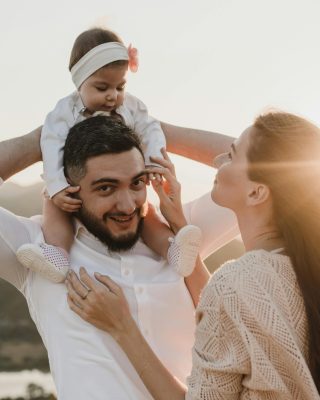 A joyful family moment with parents holding their baby outdoors at sunset.