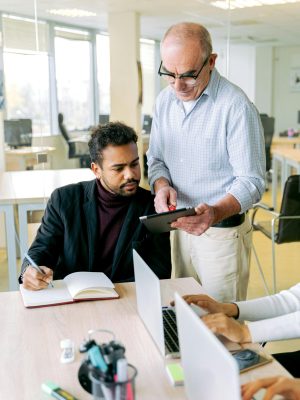 Two coworkers using a digital tablet and notebook for a teamwork session in a bright office.