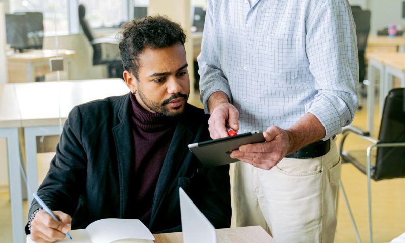 Two coworkers using a digital tablet and notebook for a teamwork session in a bright office.